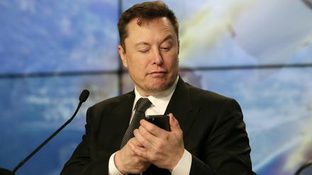 Elon Musk, Konzernchef des US-Elektroautoherstellers Tesla, schaut während einer Pressekonferenz nach dem Test einer Falcon 9 Rakete des Unternehmens auf ein Handy.  