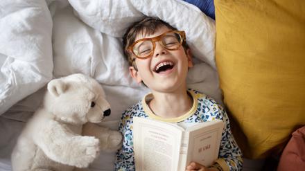 Im Bett liest es sich am besten: Ein kleiner Junge und sein Teddybär amüsieren sich prächtig. 