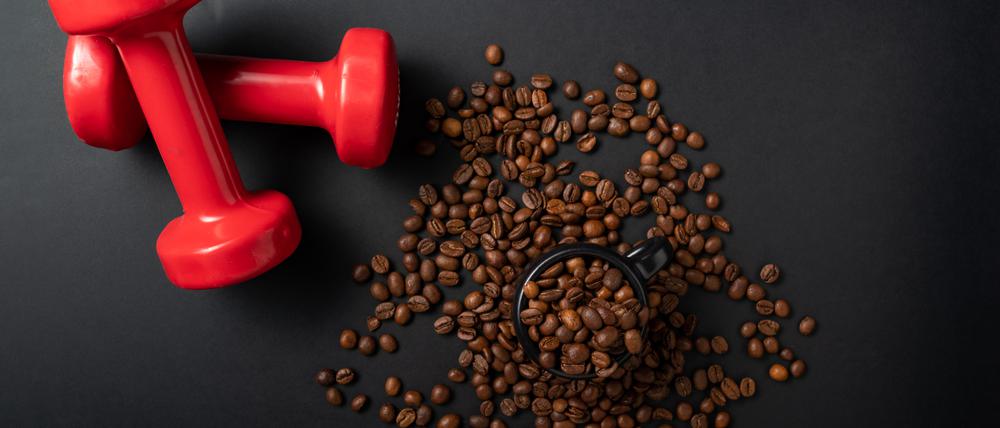 Kaffeebohnen liegen verstreut auf einem dunklen Boden, daneben zwei Kurzhanteln.