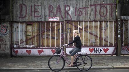 Eine blonde Frau fährt auf einem Fahrrad an dem 2010 geschlossen Club „Bar 25“ in Friedrichshain vorbei, an der das Graffito steht: „Die Bar ist tot“.