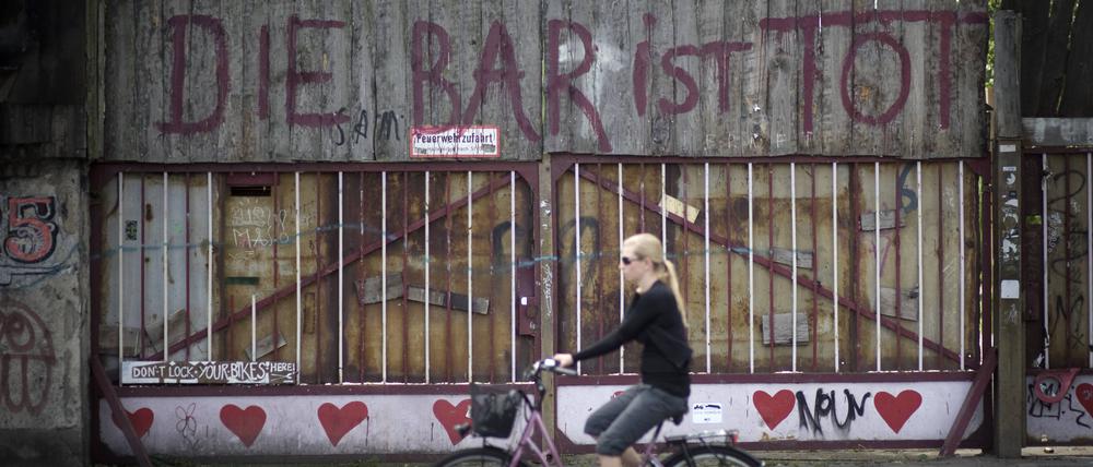 Eine blonde Frau fährt auf einem Fahrrad an dem 2010 geschlossen Club „Bar 25“ in Friedrichshain vorbei, an der das Graffito steht: „Die Bar ist tot“.