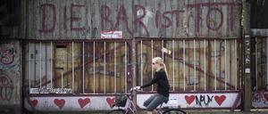 Eine blonde Frau fährt auf einem Fahrrad an dem 2010 geschlossen Club „Bar 25“ in Friedrichshain vorbei, an der das Graffito steht: „Die Bar ist tot“.