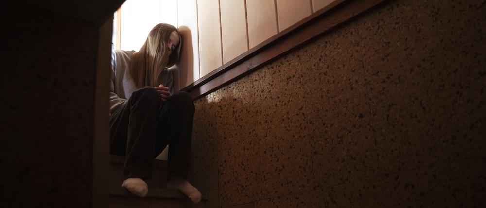 Ein Teenager sitzt auf einer Treppe und lehnt den Kopf an die Wand. Sie sieht traurig aus. 