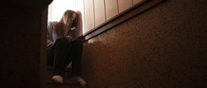 Ein Teenager sitzt auf einer Treppe und lehnt den Kopf an die Wand. Sie sieht traurig aus. 