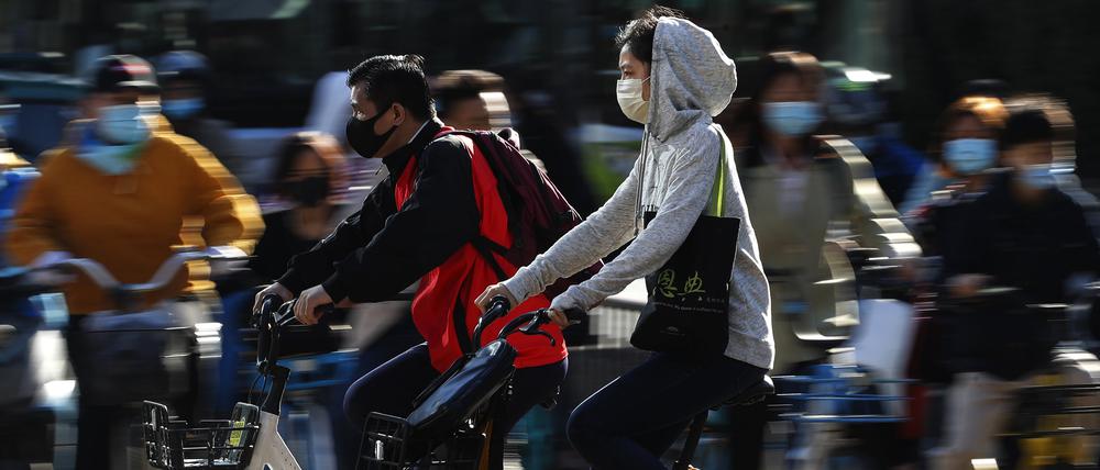 Menschen mit Gesichtsmasken fahren in Peking Fahrrad. 