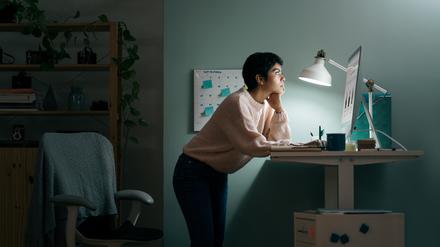 Eine junge Frau arbeitet vornübergebeugt an ihrem Stehschreibtisch.