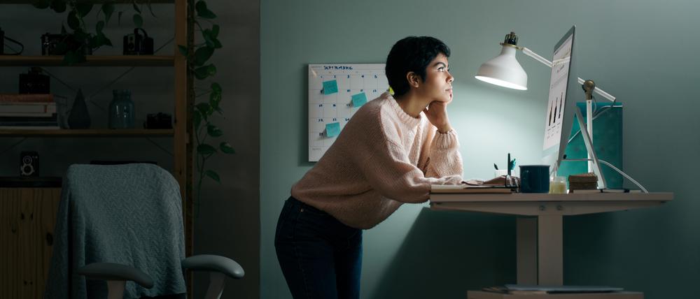 Eine junge Frau arbeitet vornübergebeugt an ihrem Stehschreibtisch.
