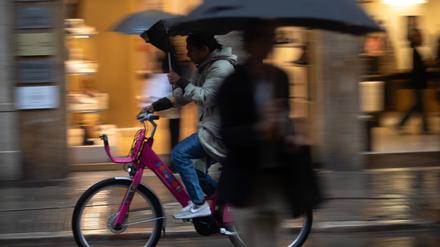Eine Person fährt mit einem Regenschirm auf einem Fahrrad in der Innenstadt von Palma während eines regnerischen Tages.