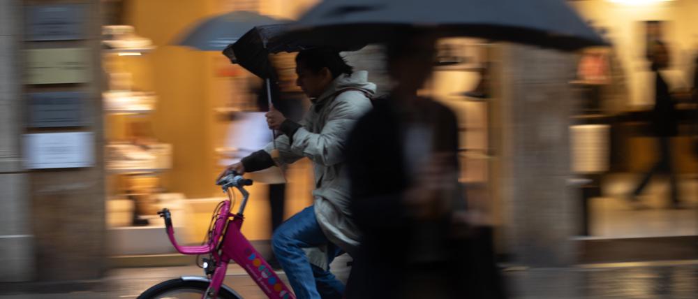 Eine Person fährt mit einem Regenschirm auf einem Fahrrad in der Innenstadt von Palma während eines regnerischen Tages.