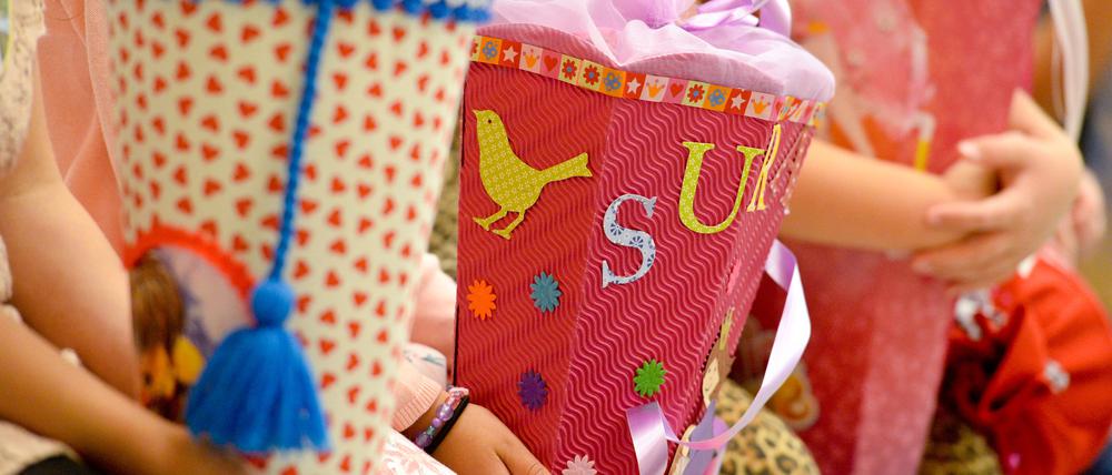 Erstklässler sitzen mit ihren Ranzen und Schultüten vor ihrer Einschulung auf einer Bank.