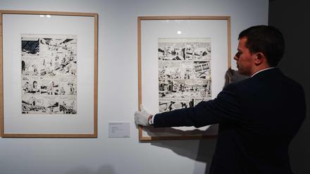 Ein Mitarbeiter des Auktionshauses hängt die zu versteigernden Originale an eine Wand.