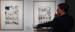 Ein Mitarbeiter des Auktionshauses hängt die zu versteigernden Originale an eine Wand.
