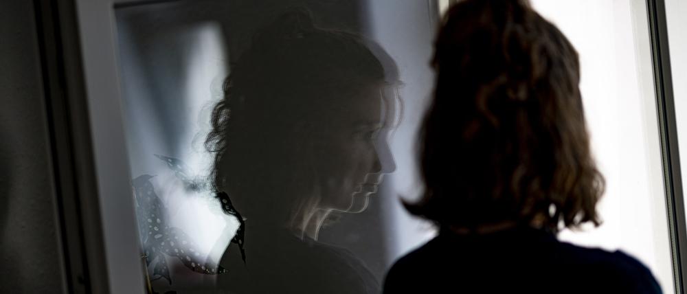 Eine Frau steht in ihrer Wohnung an einem Fenster. 