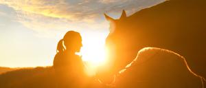 Eine junge Frau herzt ihr Pferd vor der untergehenden Sonne.