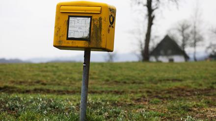 Ein Briefkasten der Deutschen Post steht auf einer Wiese am Rand einer Siedlung im Bergischen Land (NRW). 