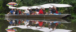 Touristen sitzen unter einer Plane vor dem Regenwetter geschützt bei einer Fahrt mit dem Spreewaldkahn über ein Fließ. 