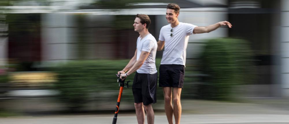 Zwei junge Männer fahren zusammen auf einem E-Scooter auf der Strasse durch Berlin snapshot-photography/R.Price *** Two young men riding together on an E Scooter on the street through Berlin snapshot photography R Price  