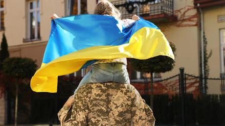 Ein ukrainischer Soldat in Militäruniform trägt seine Tochter auf den Schultern.