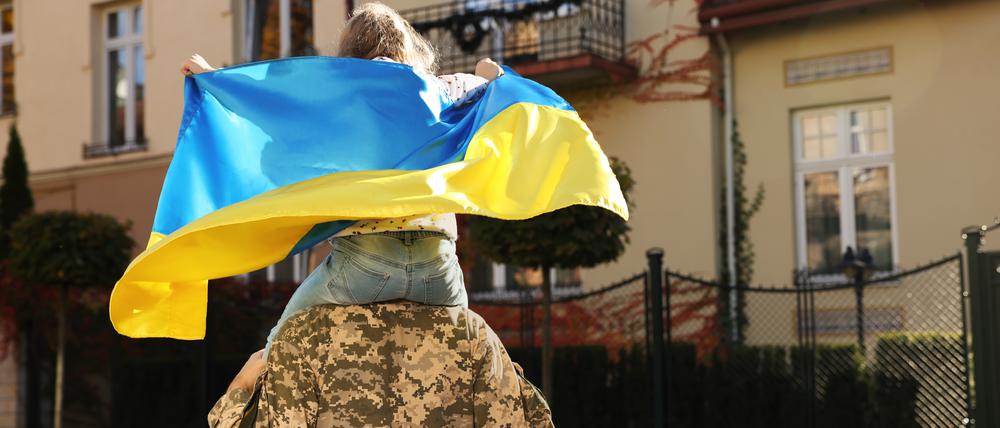 Ein ukrainischer Soldat in Militäruniform trägt seine Tochter auf den Schultern.