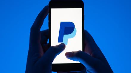 Eine Frau hält ein Smartphone mit dem Logo des Bezahldienst Paypal. 