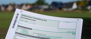 Ein Erklärung zur Feststellung des Grundsteuerwerts für das Jahr 2025 wird vor einer Wohnsiedlung hochgehalten. 
