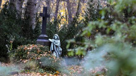 Eine Figur und ein Kreuz an einem Grab auf dem St. Elisabeth-Friedhof.