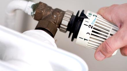 Eine Frau dreht am Thermostat eines Heizkörpers. 