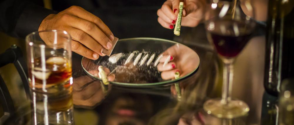 Woman's hand holding rolled dollar with man cutting cocaine line on table. Horizontal shot.