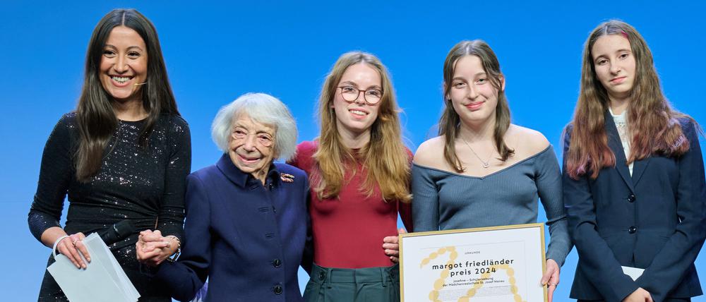 Margot Friedländer (2.v.l) übergibt Schülerinnen der Schülerzeitung „josefine“ den Margot Friedländer Schulpreis 2024, während Moderatorin Alev Doğan (l) ihre Hand hält.