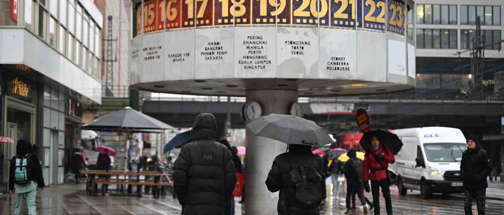 Passanten laufen mit Regenschirmen vor der Weltzeituhr am Alexanderplatz.