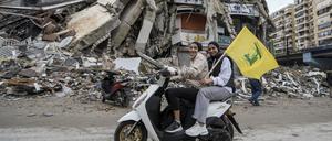 Frauen auf einem Motorroller halten eine Hisbollah-Fahne, während sie an einem zerstörten Gebäude vorbeifahren.