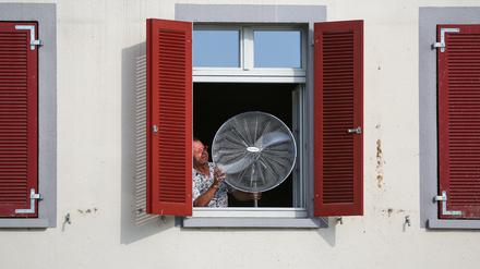 Ein Mann stellt im August 2023 einen Ventilator an sein geöffnetes Fenster. 