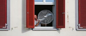 Ein Mann stellt im August 2023 einen Ventilator an sein geöffnetes Fenster. 