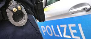 Ein Polizist mit Handschellen und einer Pistole am Gürtel steht vor einem Streifenwagen. (Symbolbild) 
