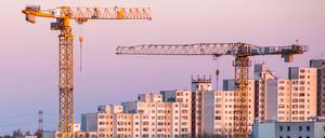 Baukräne leuchten vor einer Wohnsiedlung golden im Licht der aufgehenden Sonne. Das Bündnis für Wohnungsneubau und bezahlbares Wohnen stellt am Montag vor, worauf sich die Teilnehmer nach monatelangen Verhandlungen geeingt haben. (zu dpa «Fertig für die Unterschrift: Wohnungsbündnis präsentiert Ergebnisse») +++ dpa-Bildfunk +++