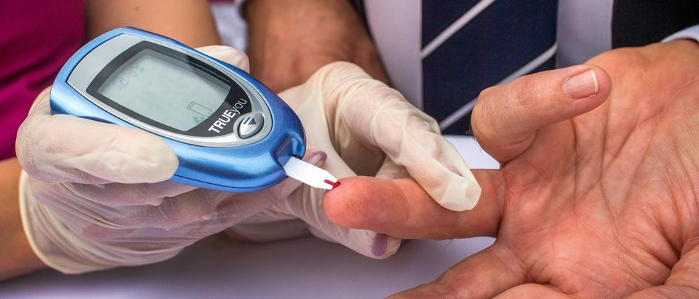 Ein Mann lässt sich von einer Diabetesberaterin eine Blutprobe für einen Blutzuckertest nehmen.