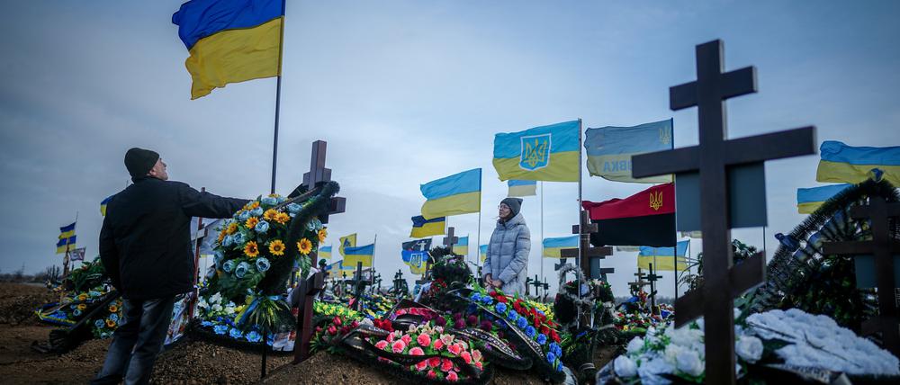 Anna, die Ehefrau eines vor zwei Monaten getöteten Soldaten, und der Vater Oleksandr stellen auf dem Friedhof der Hafenstadt Odessa die ukrainische Nationalflagge am Grab ihres Ehemannes auf.