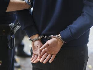 Ein Mann trägt Handschellen und wird von einem Polizisten abgeführt. (Symbolbild)