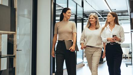 Drei Business-Frauen laufen beschwingt durch einen Flur. 
