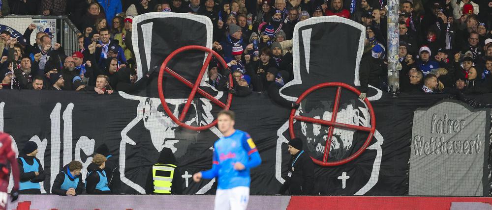 Banner im Kieler Fanblock zeigen die Gesichter von Oliver Mintzlaff und Jürgen Klopp mit einem Fadenkreuz darüber.