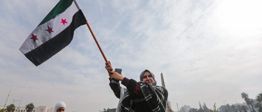 Eine Frau hält in Damaskus die syrische Oppositionsflagge und feiert.