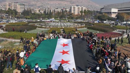 Menschen halten eine Flagge der syrischen Revolution am Umayyad-Platz in Damaskus.