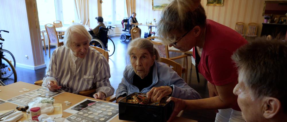 Bingo-Runde im Franz-Jordan-Stift in Berlin-Reinickendorf. Drei Frauen sitzen am Tisch mit den Bingo-Karten. Eine von ihnen nimmt sich ein Tütchen Gummibären.