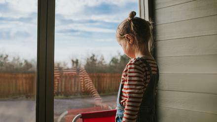 Ein kleines Mädchen schaut aus dem Fenster. Schon vermeintlich „harmlose“ Konflikte können Kinder stark belasten – oft ohne dass Eltern es merken. 
