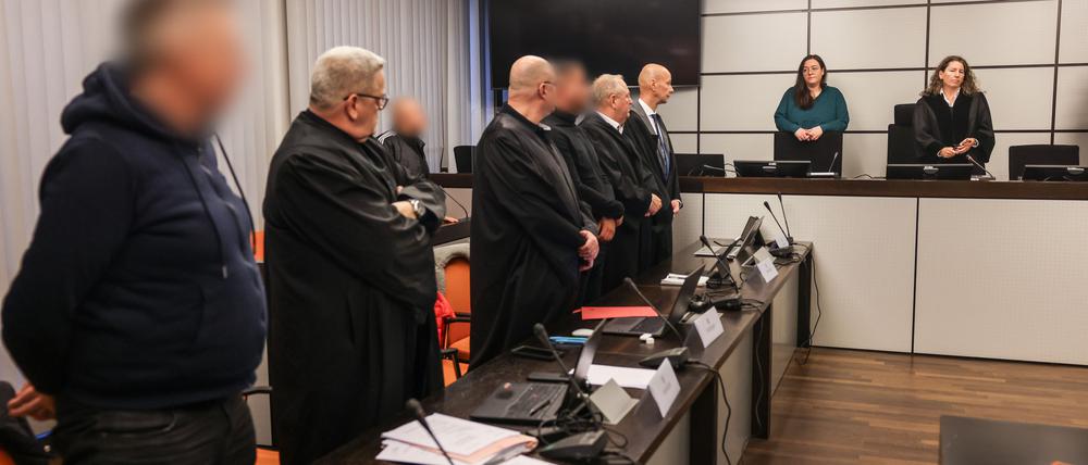 10.12.2024, Nordrhein-Westfalen, Wuppertal: Die Angeklagten und ihre Anwälte stehen beim Einzug der Richterin Birgit Neubert (r) auf. In Wuppertal hat der Prozess wegen eines Erpressungsversuchs gegen die Familie von Ex-Formel-1-Weltmeister Michael Schumacher begonnen. Angeklagt sind drei 30 bis 53 Jahre alte Männer. Dem Haupttäter wird versuchte Erpressung in einem besonders schweren Fall vorgeworfen, den beiden anderen Beihilfe dazu.