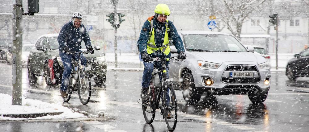 Autos und Fahrradfaher unterm Schneefall in Berlin am 16. Januar 2024.