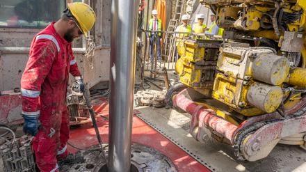 Arbeiter hantieren an einer Geothermiekraftwerk-Baustelle mit einem Bohrgestänge. 