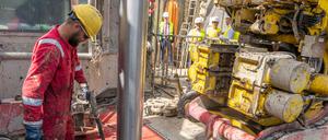 Arbeiter hantieren an einer Geothermiekraftwerk-Baustelle mit einem Bohrgestänge. 