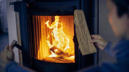 Eine Frau wirft ein Holzscheit in einen Kaminofen.