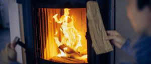 Eine Frau wirft ein Holzscheit in einen Kaminofen.
